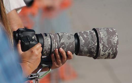 A female photographer holding a Canon brand camera at Aviation Nation 2019. The lens has a digital camo lens covering