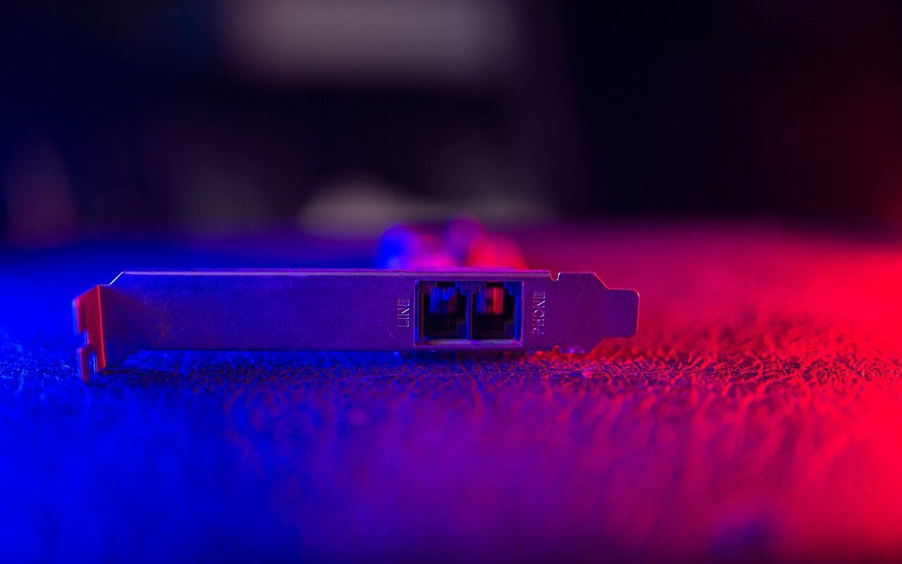 Network interface card positioned on a textured surface while illuminated by red and blue lights, showcasing its ports and structure in a visually…